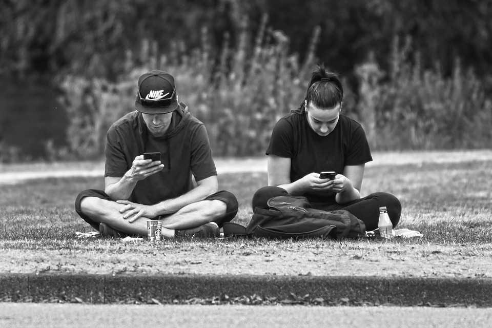 Two teenagers sitting in the park using mobile phones.